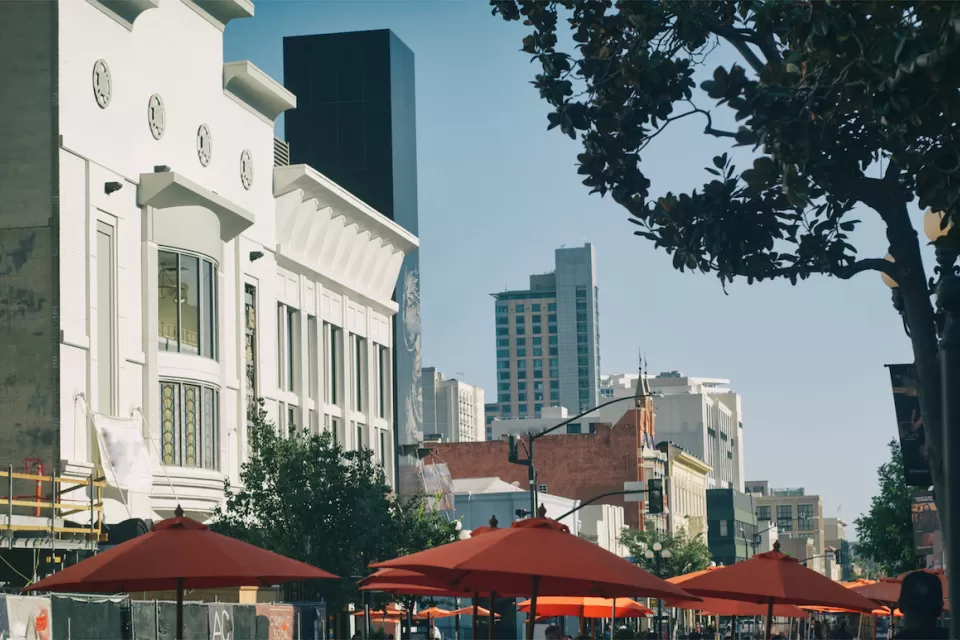 The tops of umbrellas for outdoor dining spaces are visible with large buildings in the background on a sunny day in the city of San Diego.
